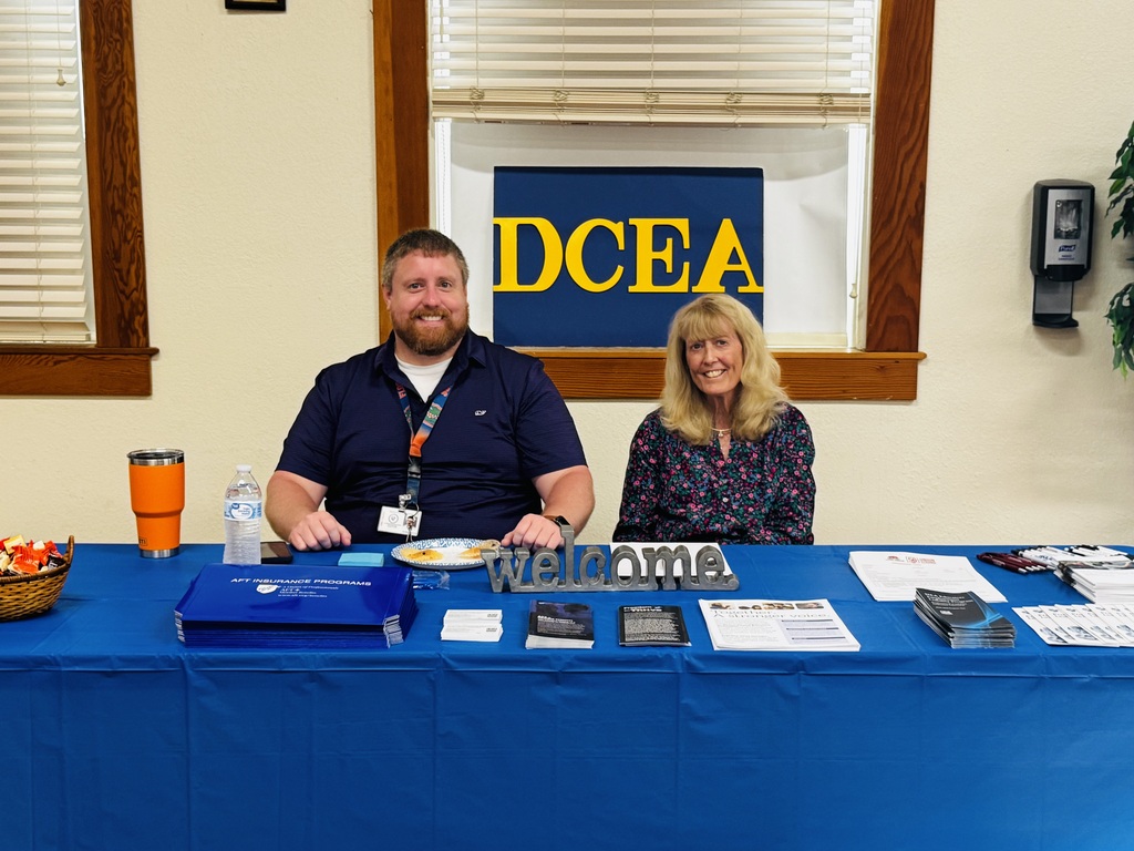 man and woman sitting at table with DCEA banner and welcome