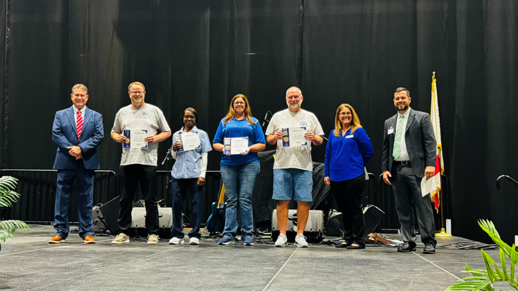 group of staff being recognized on stage for years of service smiling and posing for a picture