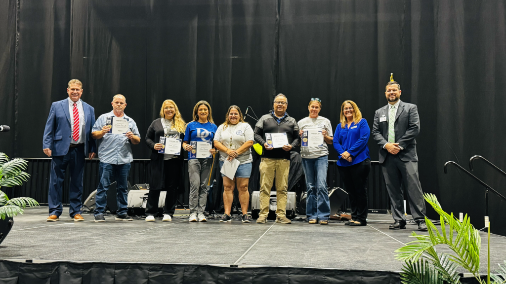group of staff being recognized on stage for years of service smiling and posing for a picture