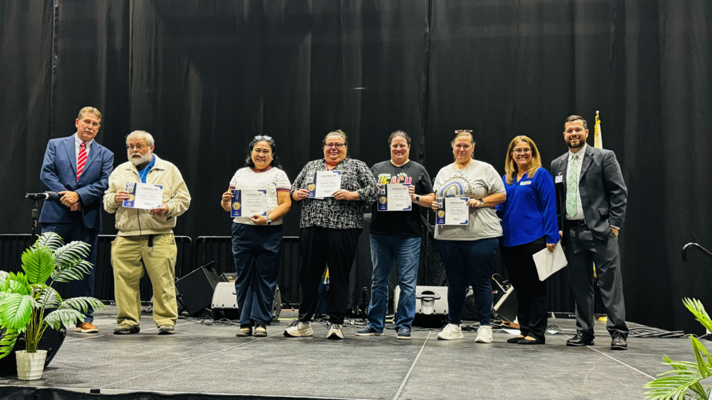 group of staff being recognized on stage for years of service smiling and posing for a picture