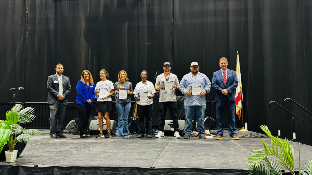 group of staff being recognized on stage for years of service smiling and posing for a picture