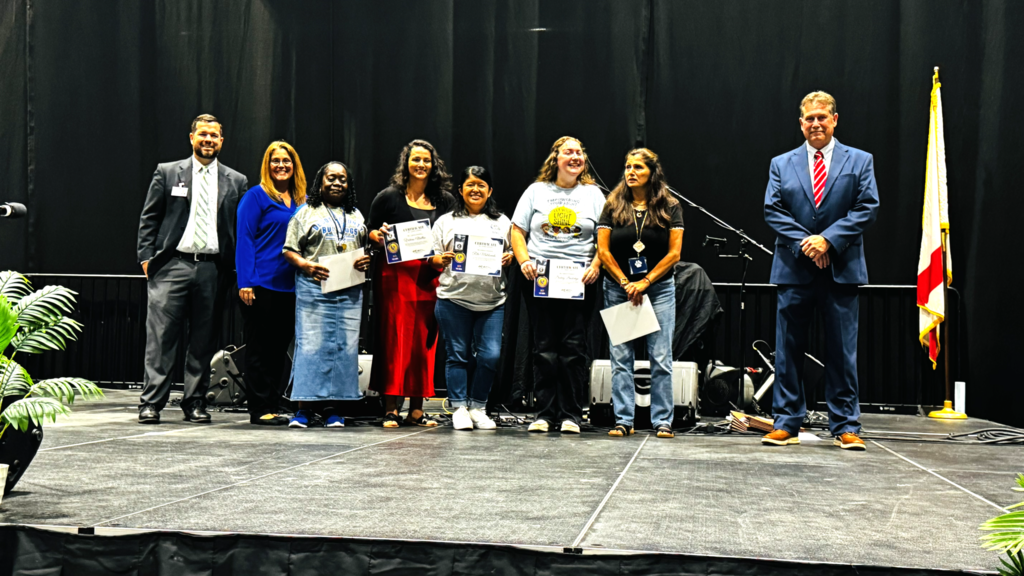 group of staff being recognized on stage for years of service smiling and posing for a picture