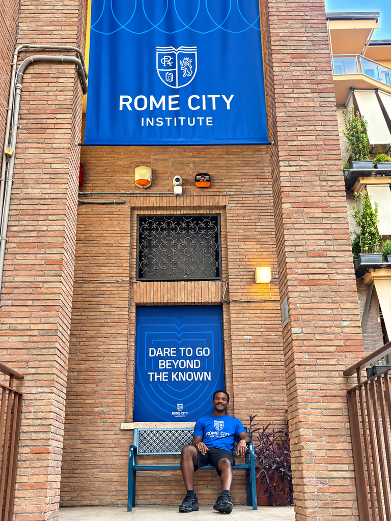 man wearing a blue shirt sitting on a bench in front of a  building with a sign "Rome City Institute"