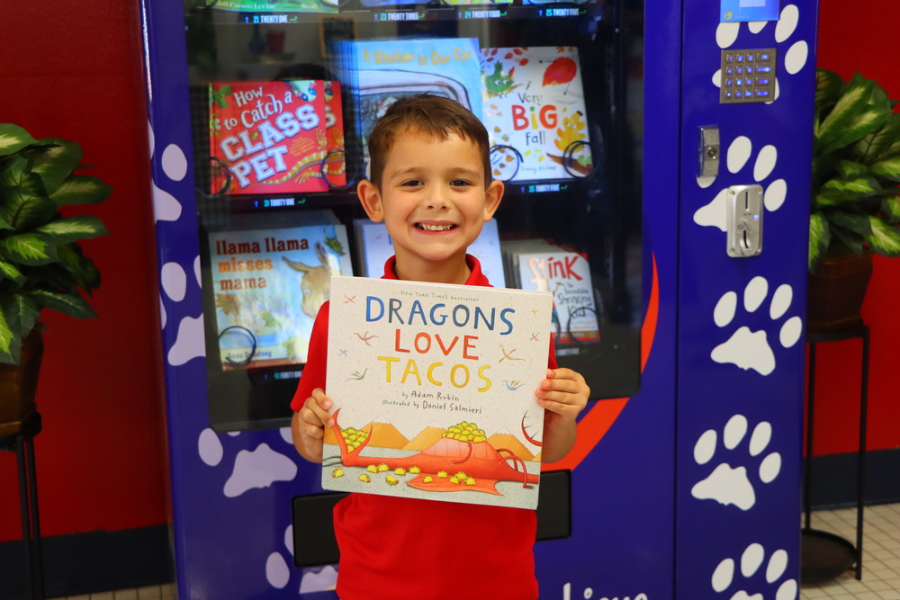 Child holding a book in front of book vending machine