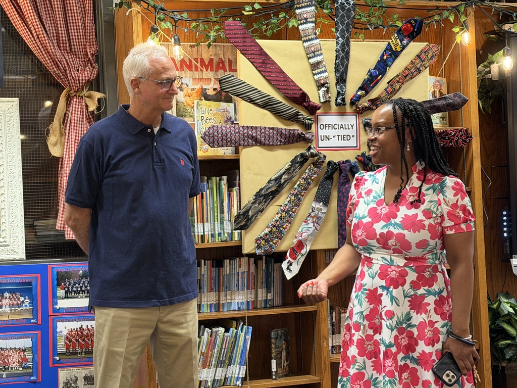 A man and a woman are standing in front of a bookshelf with ties arranged in a decorative design.