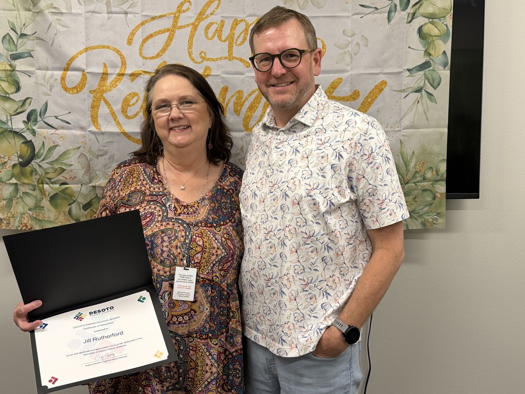 Man and woman standing in front of a banner. The woman holds a certificate. Both are smiling.