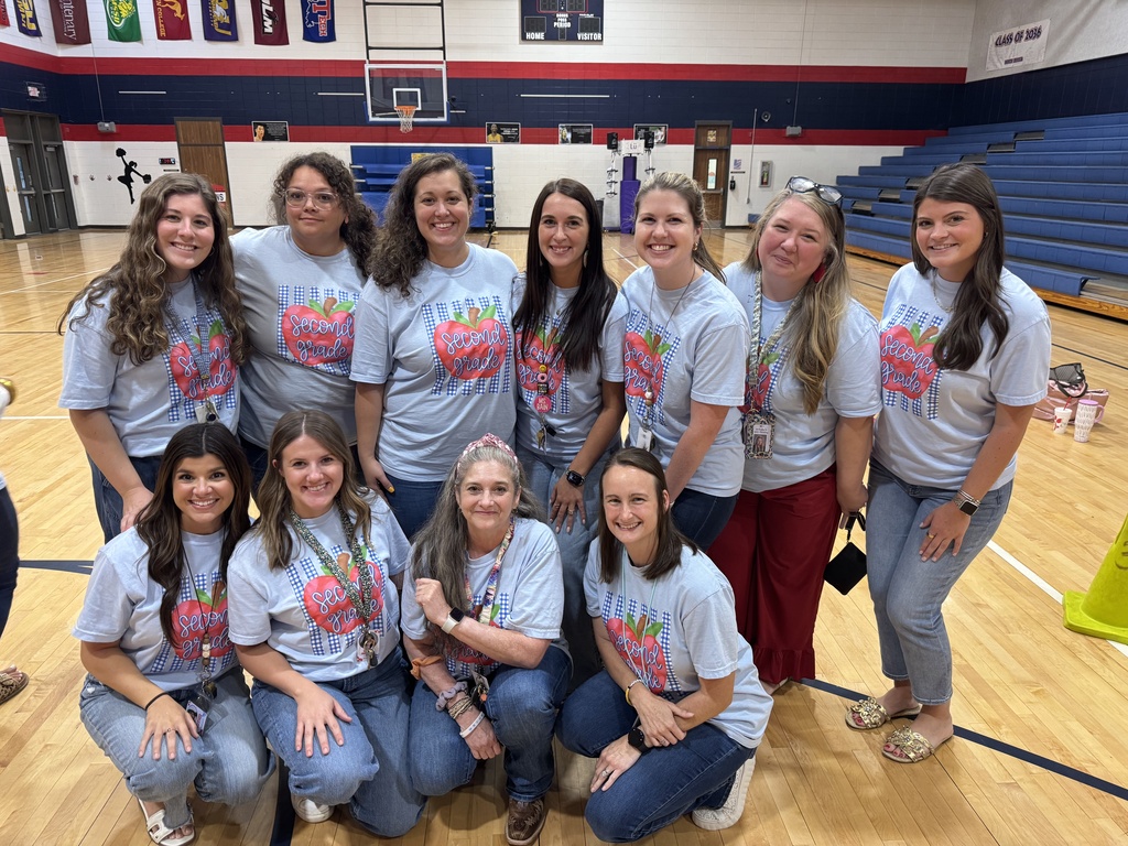 A group of women in matching shirts stands in a basketball court. They are smiling and posing for a photo.