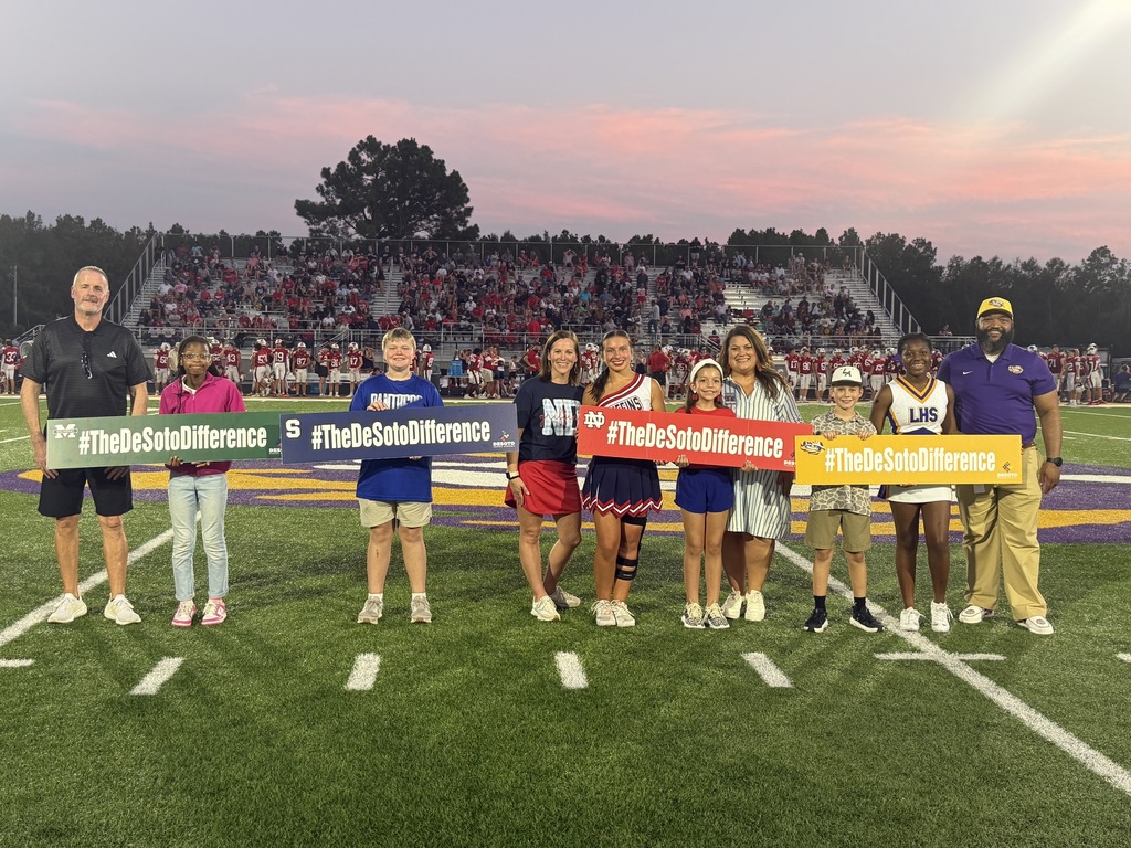 Group of people on a field holding signs with the text "#MakeTheDifference" at a sports event.