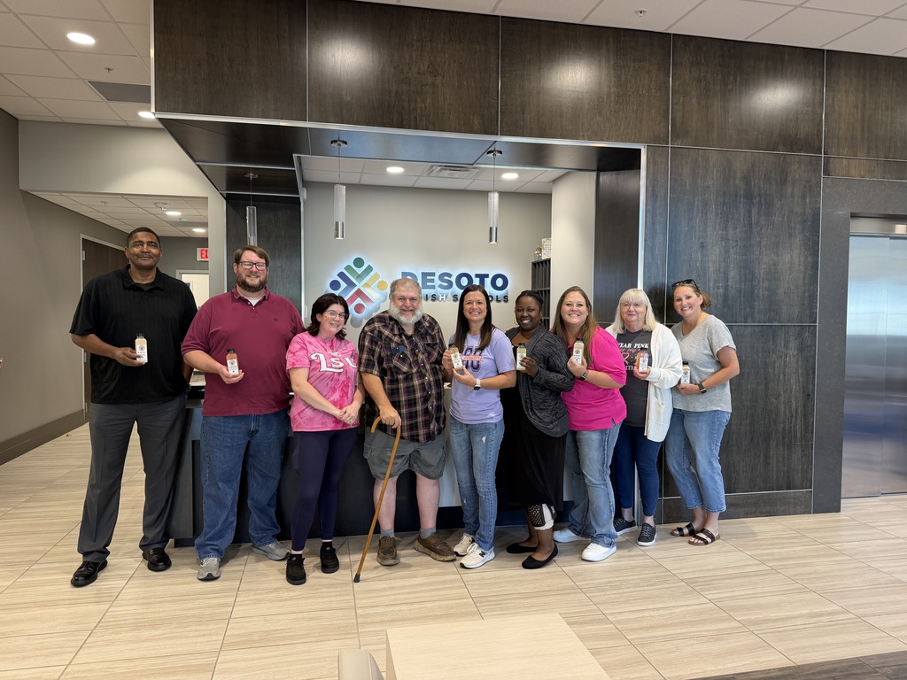 People stand in a lobby. Some hold cups and a sign is in the background.