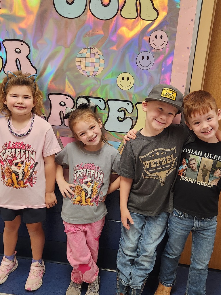 Four children stand in a row, smiling at the camera. The backdrop features colorful letters and smiley faces.