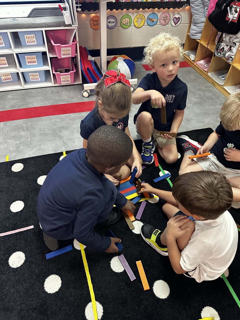 Five young children sitting on a carpeted floor. They are engaged in a hands-on activity with colorful plastic tools.