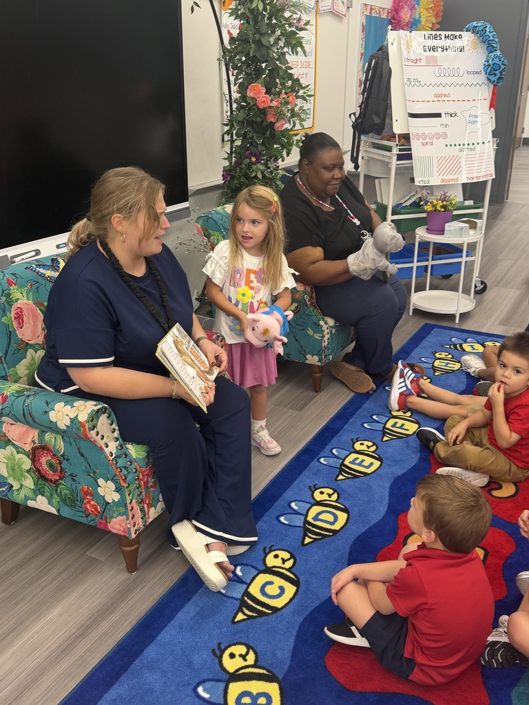 Woman sits on couch with children. One reads from a book. Children sit on floor.