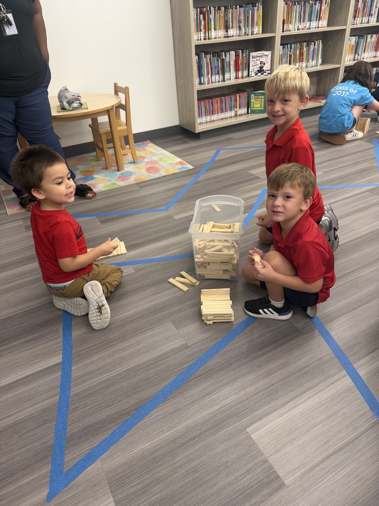 Three young boys are playing with blocks in a classroom. One boy holds a wooden block.