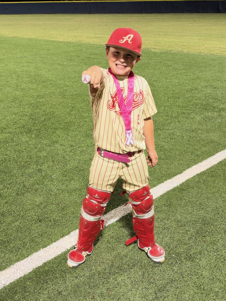 Young boy in sports uniform standing on green field pointing finger, smiling. White line on field.