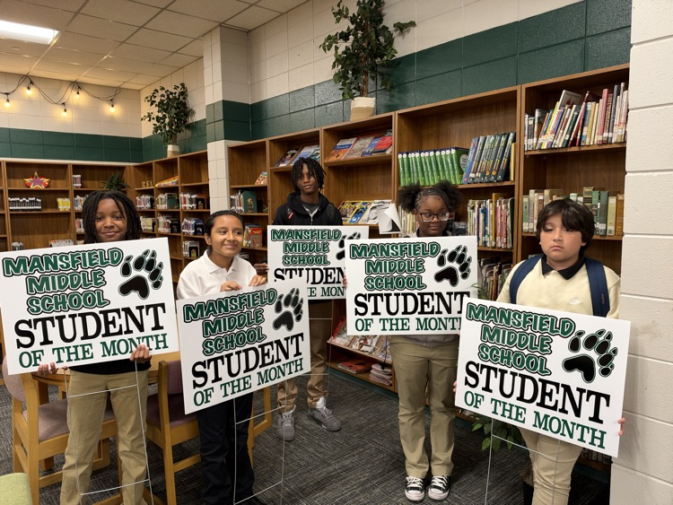 Five students hold signs that say "Student of the Month" in a room with bookshelves.