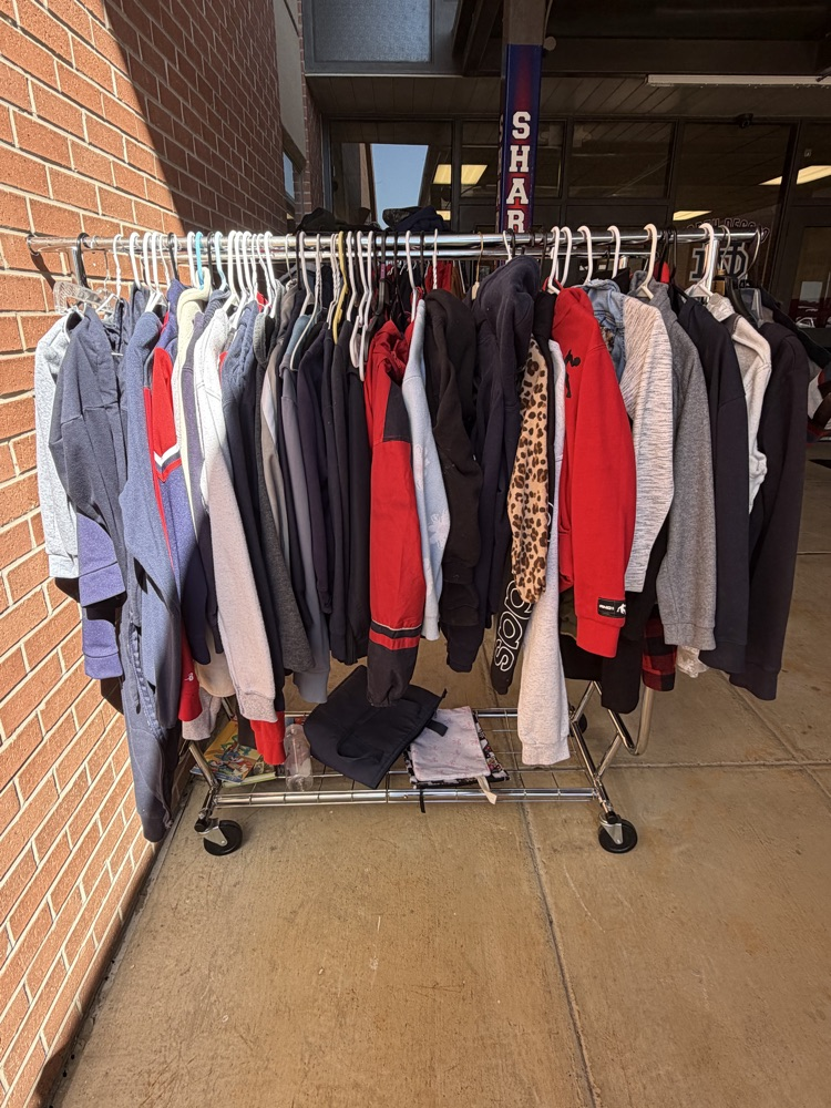 A row of various winter clothes on hangers outside a school building.