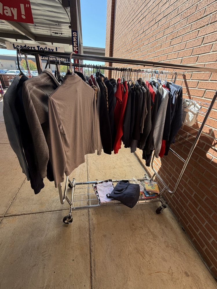Clothes on a rolling rack outdoors, near a brick wall and sidewalk; a red banner with white text is visible.