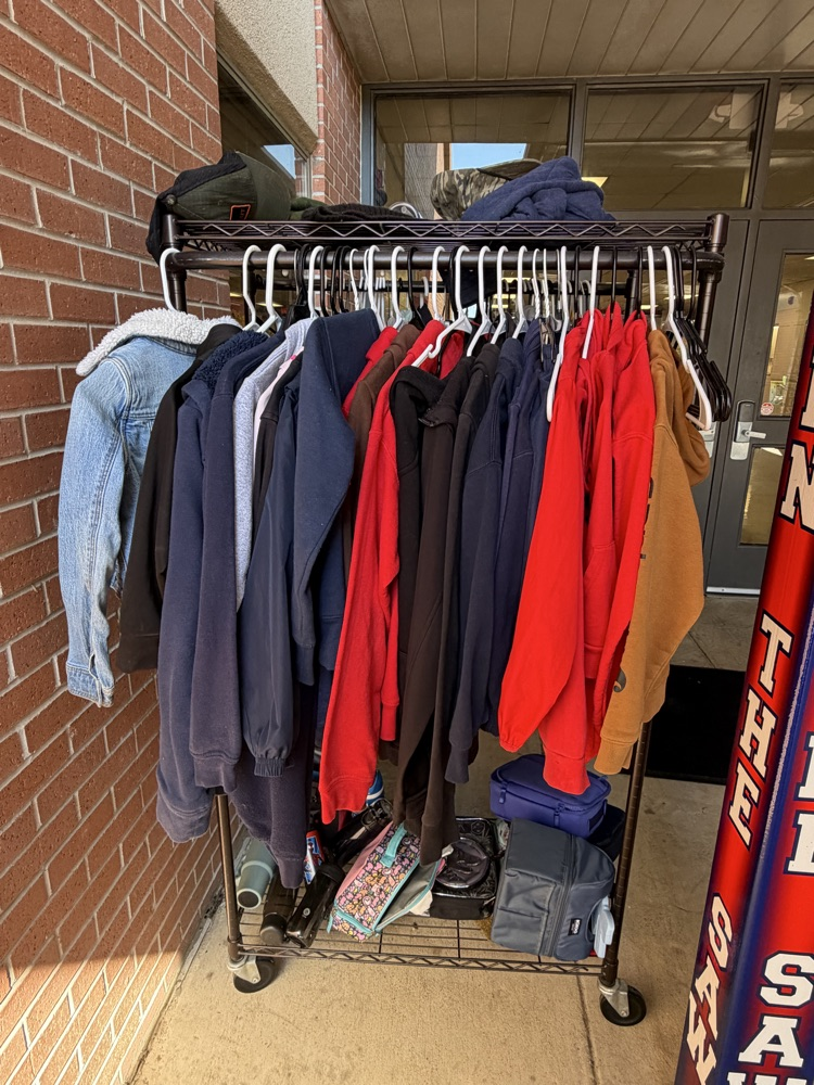 Clothing items on a wheeled rack in front of a brick wall, near a door.