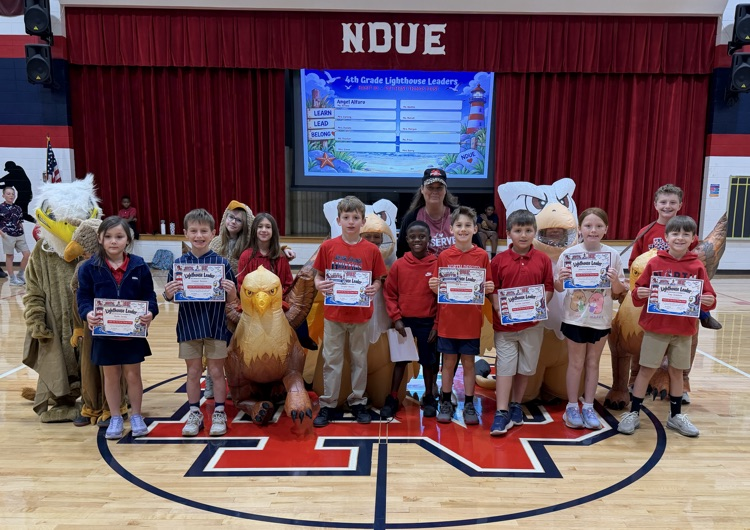 A group of young children holding certificates, with a mascot, on a basketball court.
