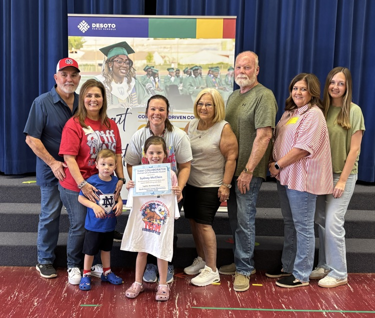 Several adults and children pose for a photo with a child holding a certificate in front of a stage.