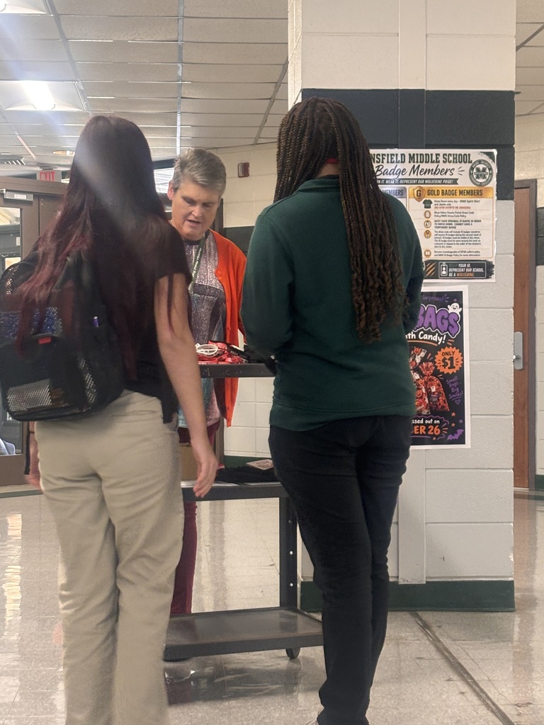 Three students standing by a table with a small item on it in a corridor.