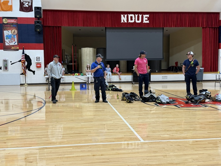 Several people in hats stand on a basketball court with bags and cones in the foreground.