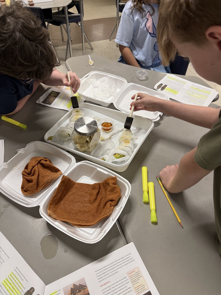 Two children using brushes on a tray with a jar, towel, and a piece of paper.