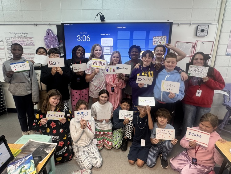 A classroom with students holding signs and posing for a photo in front of a screen.