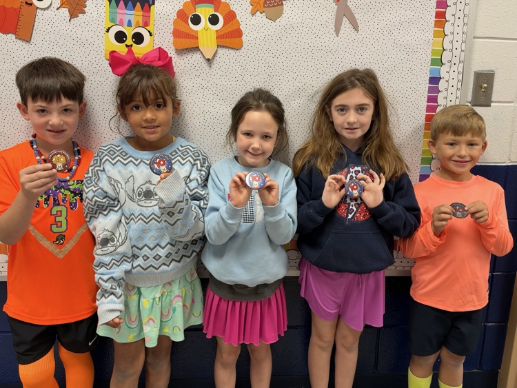 Five young children wearing medals stand in front of a colorful bulletin board.