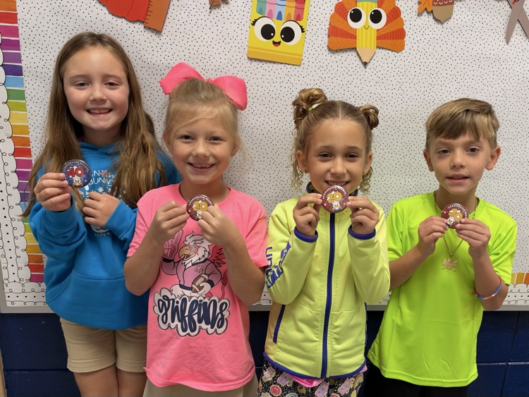 Four young children standing close together in front of a bulletin board with colorful decorations.