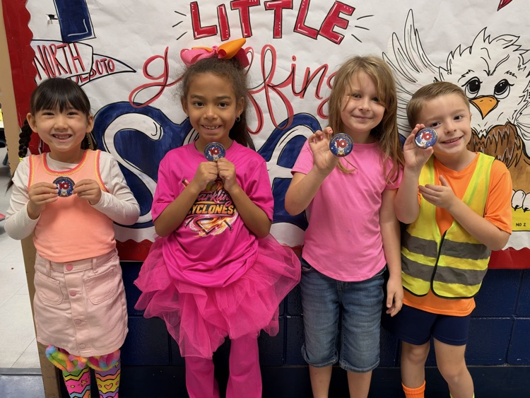 Five children standing in a line, each holding a small object, with a banner in the background.