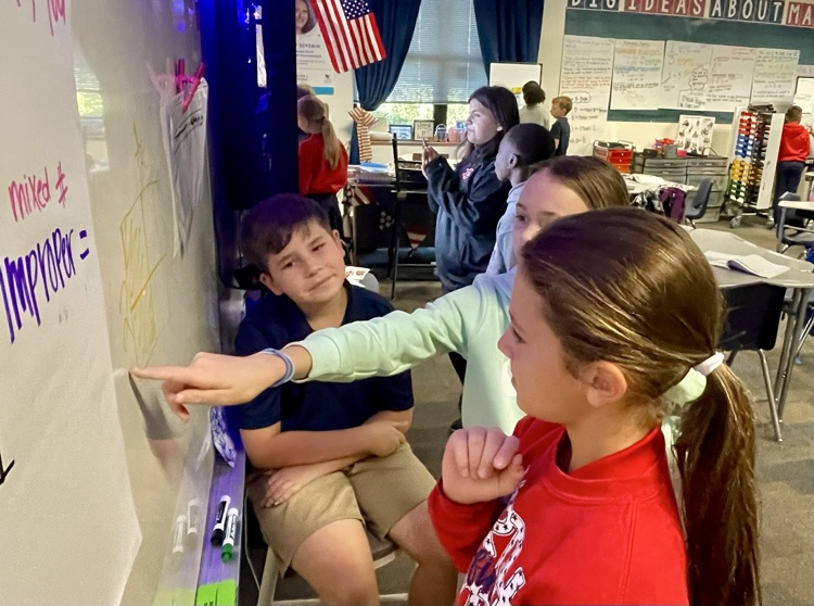 Children at a board with one pointing at a word written in purple marker.