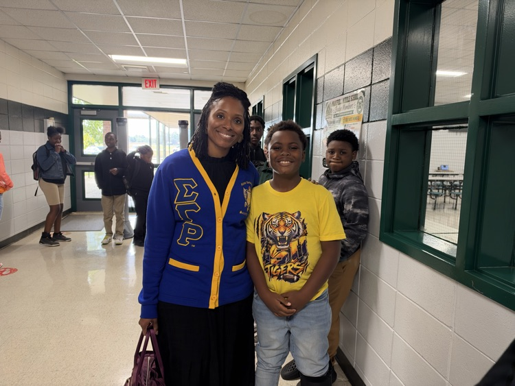 A woman and a boy stand in a school hallway. The boy wears a yellow shirt with a tiger.