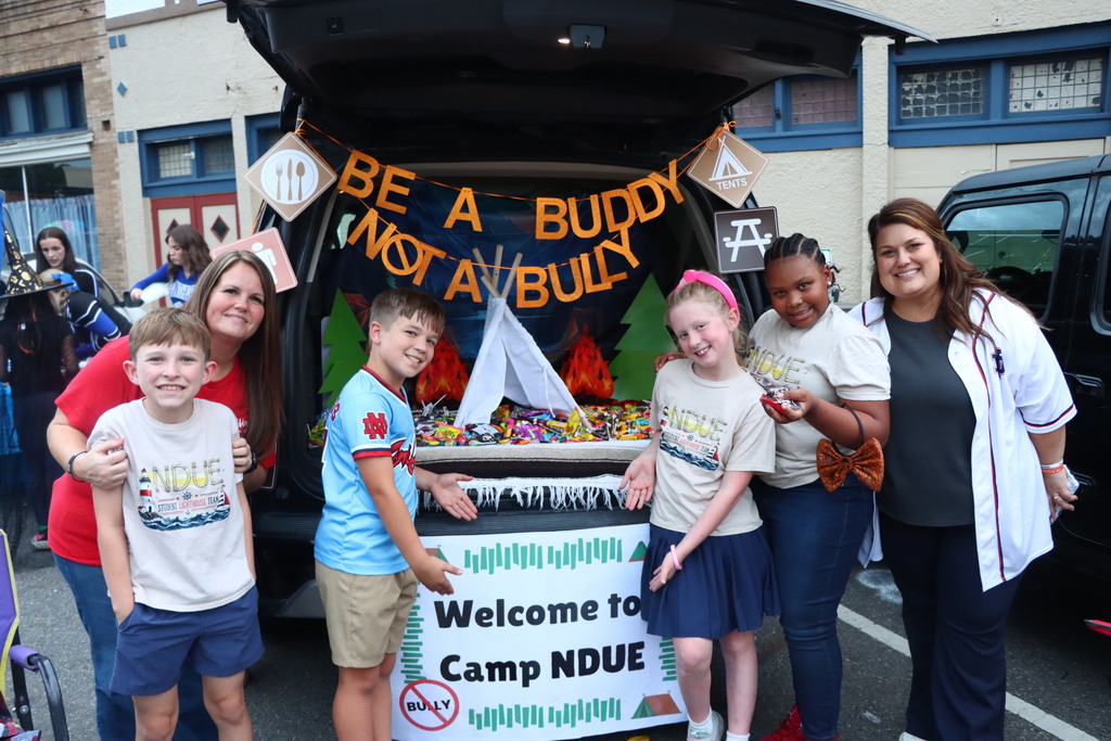 A group of six people posing in front of a car decorated with a banner.
