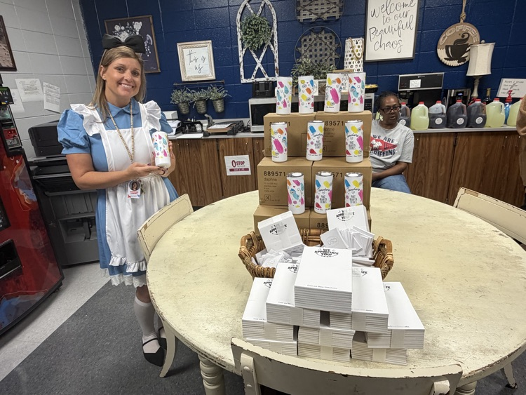 Woman in costume holds a box near table with stacks of white boxes and colorful containers.