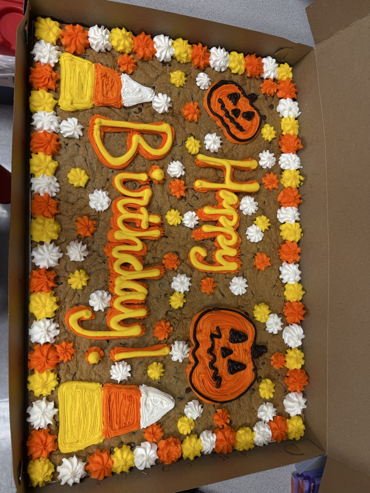 Cake in box, decorated with Halloween pumpkins, candy corn, and flowers, with text "Happy Birthday!"