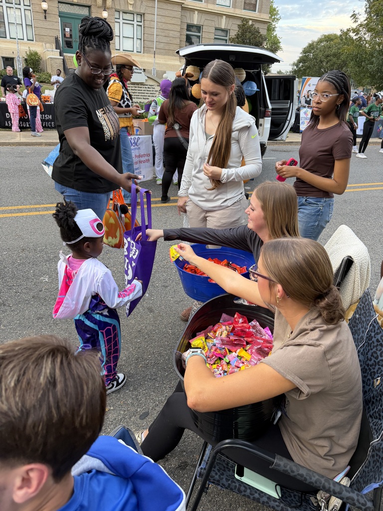 Adults and children at a street fair with a woman holding a candy bucket and a girl in a costume.
