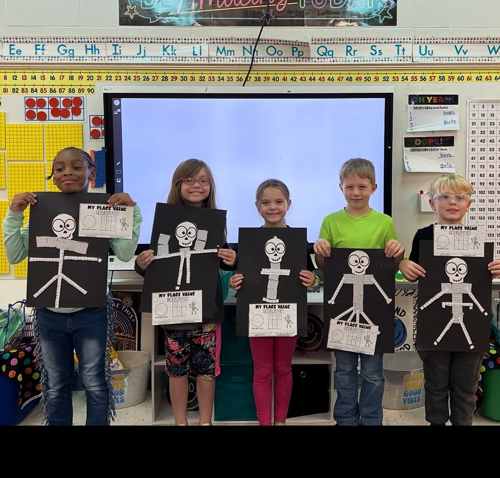 Students holding place value skeletons in front of a smart board and white board