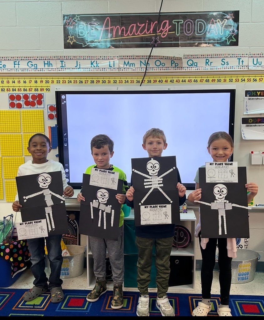 Students holding place value skeletons in front of a smart board and white board