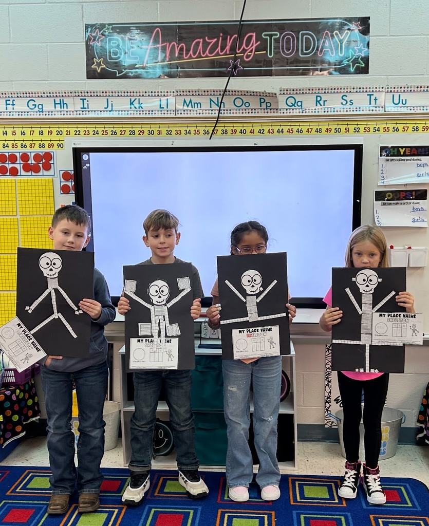 Students holding place value skeletons in front of a smart board and white board