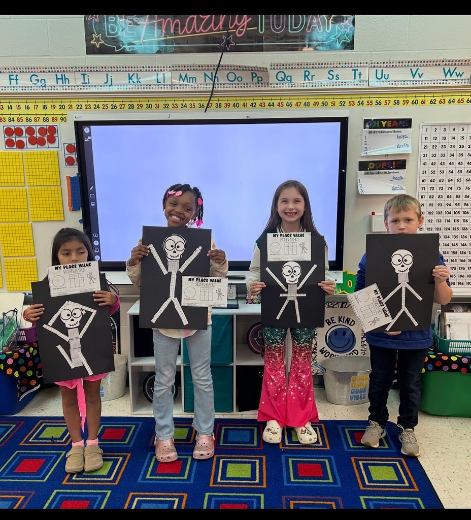 Students holding place value skeletons in front of a smart board and white board
