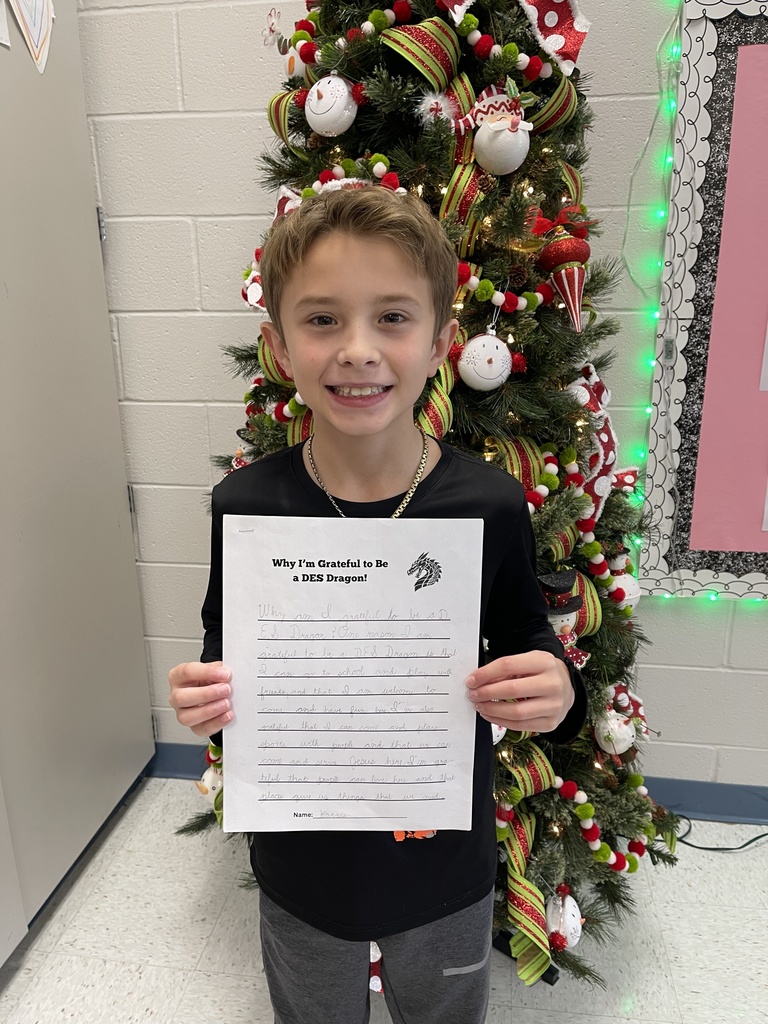 Male student in front of a decorated christmas tree, wearing a black shirt, denim pants and holding a writing prompt
