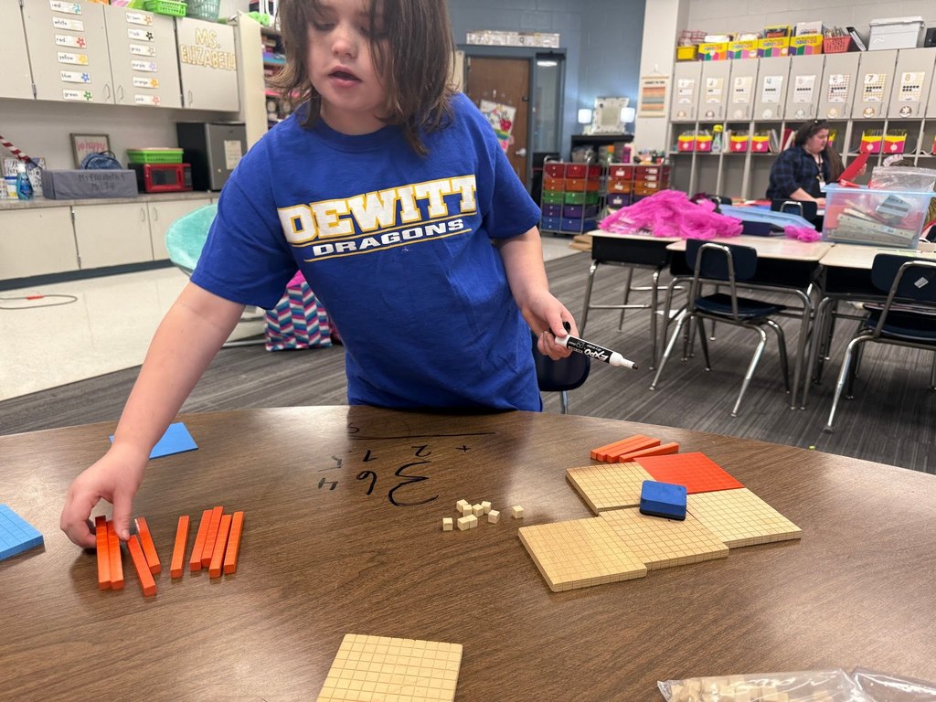 female student using math manipulatives wearing a blue dewitt dragon shirt in a classroom and standing at a table