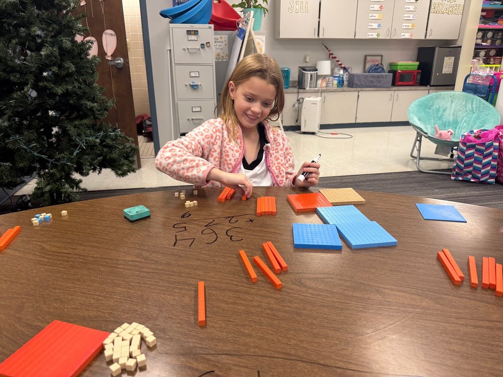 female student using math manipulatives wearing a pink and white shirt in a classroom with a christmas tree in the background