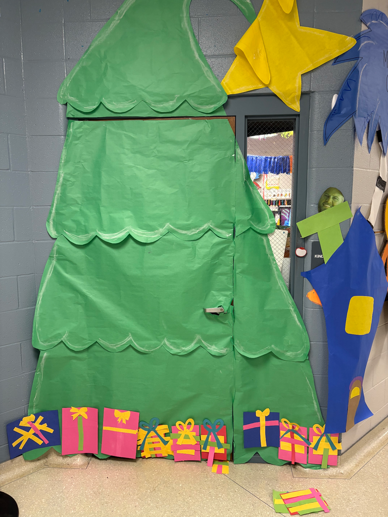 A classroom door decorated like a giant Christmas Tree, with a giant yellow star and presents under the tree