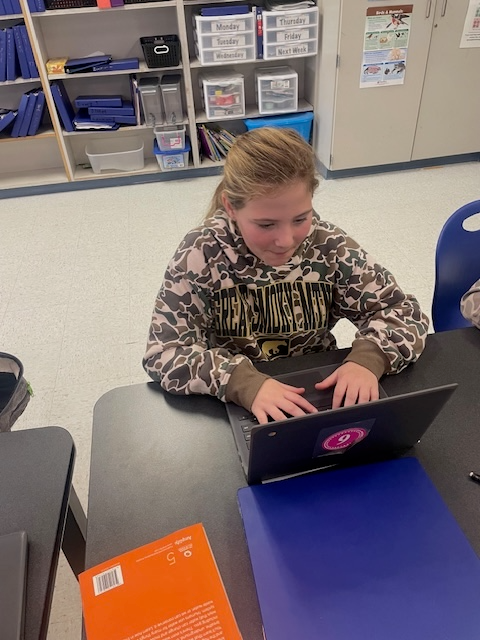 Female student with blonde hair wearing a camo sweatshirt working on a laptop computer