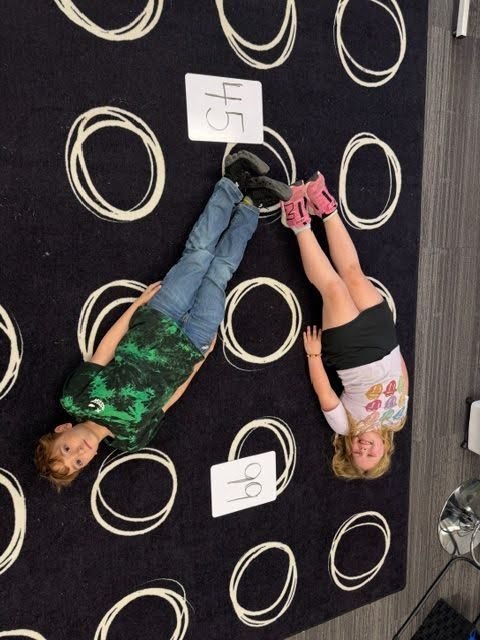 Students creating math greater than, less than or equal value signs with their bodies on the floor