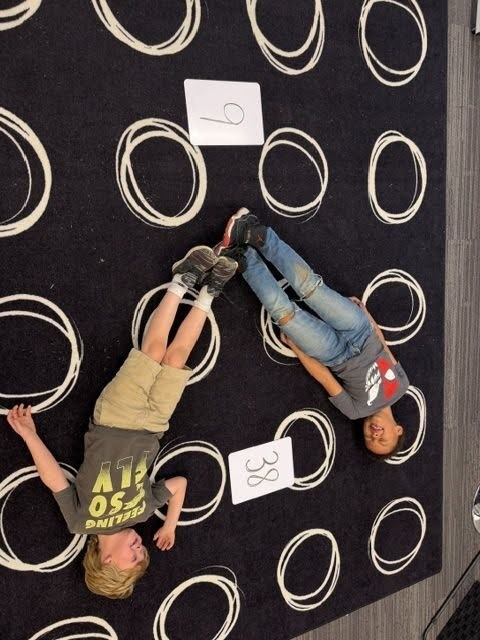 Students creating math greater than, less than or equal value signs with their bodies on the floor