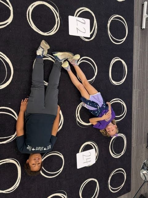 Students creating math greater than, less than or equal value signs with their bodies on the floor