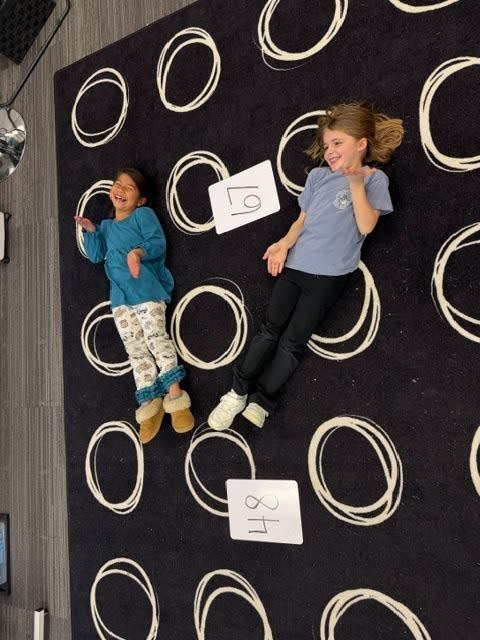 Students creating math greater than, less than or equal value signs with their bodies on the floor